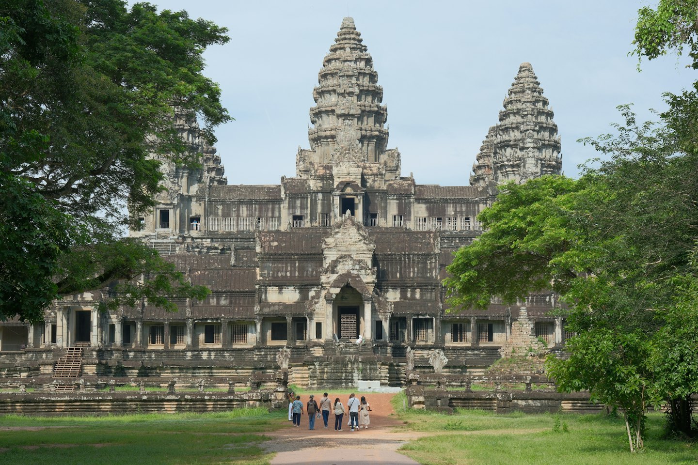 Tourists walk along a dirt path toward a stone temple.