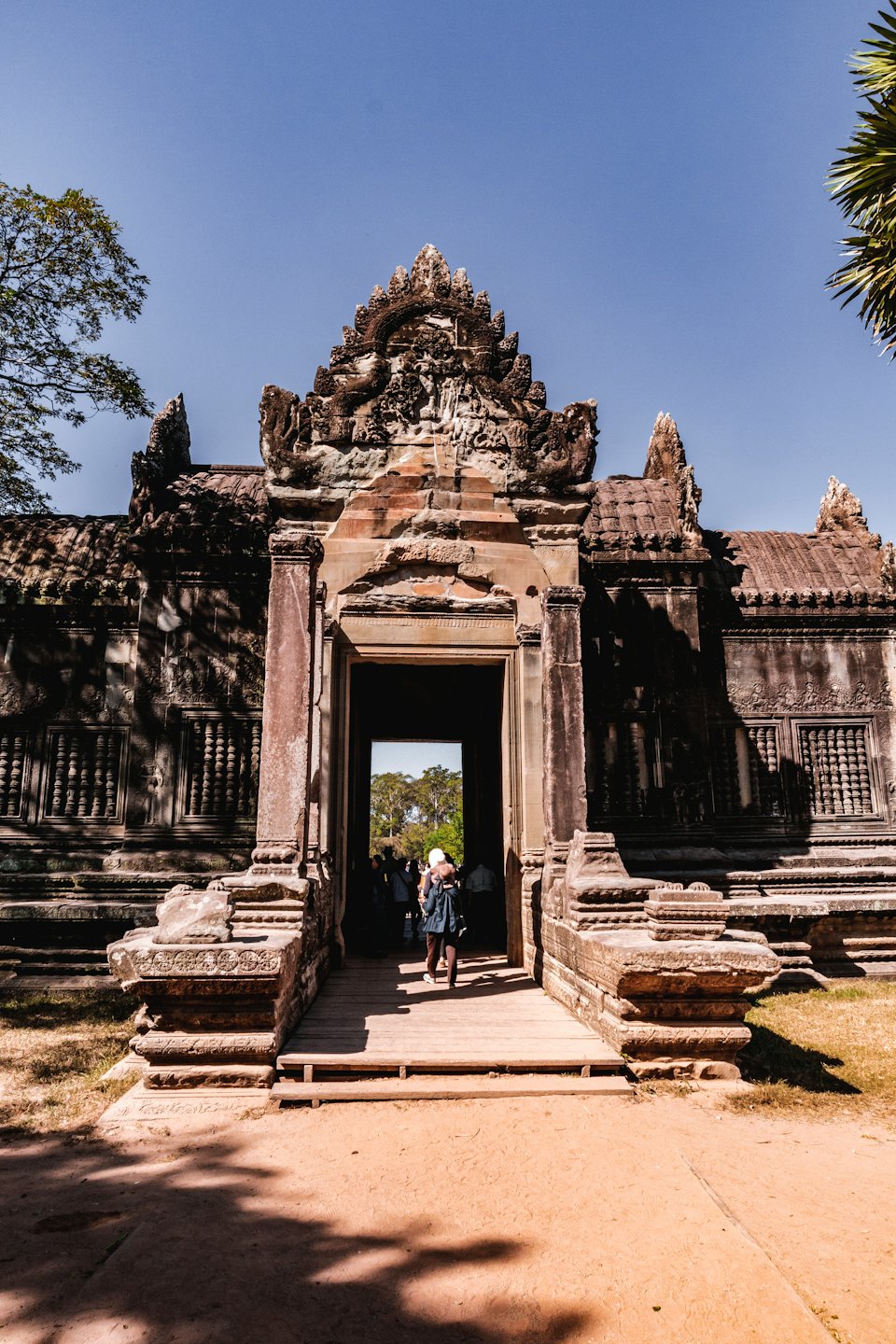 Tourists enter a sunlit ancient stone temple with carved details.